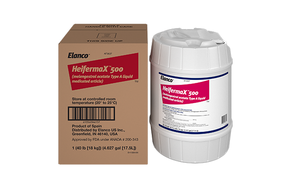 A brown cardboard shipping carton next to a large white plastic tub of Elanco HeifermaX 500 (melengestrol acetate Type A liquid medicated article). Both feature a white and magenta label.
