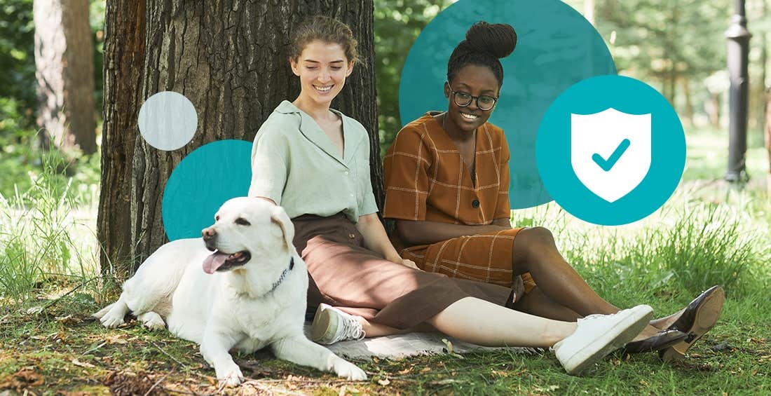 Yellow lab and two women sitting under a tree