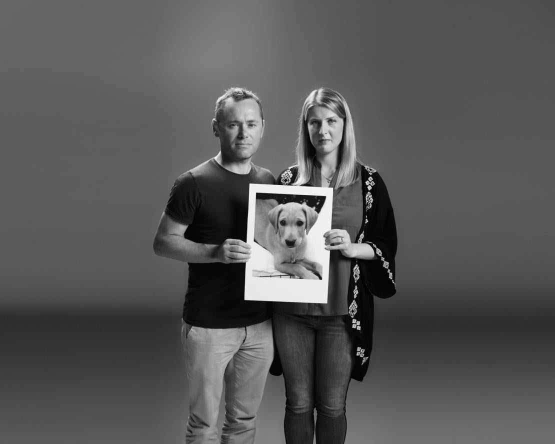 Husband and wife holding image of dog. 