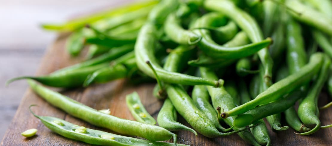 A pile of fresh green beans on a cutting board.